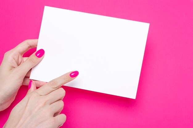 Mão feminina segurando um pôster a5 em branco sobre fundo rosa