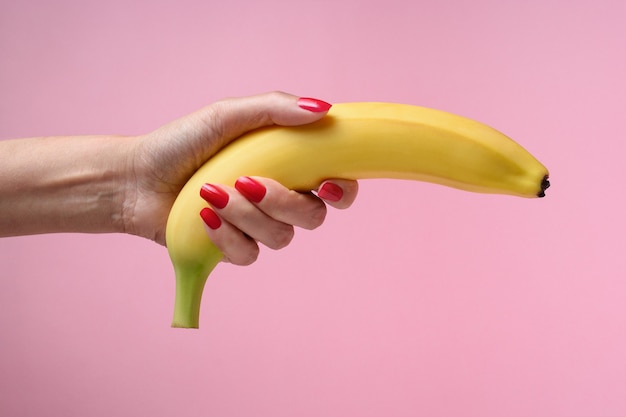 Mão feminina segurando uma banana isolada em uma rosa