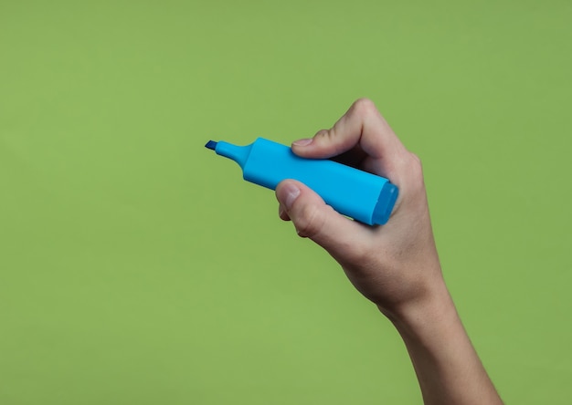 Mão feminina segurando uma caneta hidrográfica azul em um papel verde