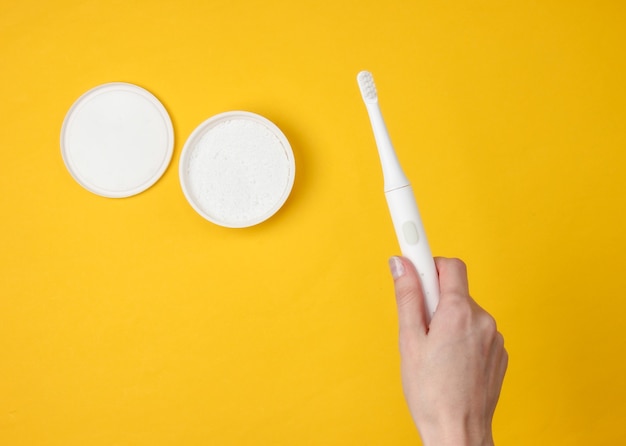 Mão feminina segurando uma escova de dentes elétrica moderna e pó dental amarelo