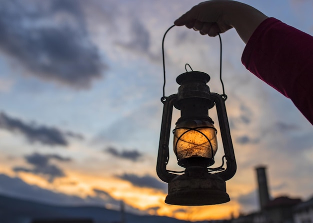 Foto mão feminina segurando uma lanterna com o belo pôr do sol ao fundo