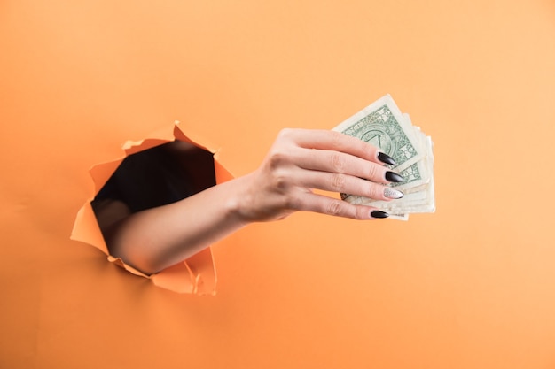 Mão feminina segurando uma nota de um dólar em um fundo laranja