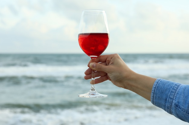 Mão feminina segurando uma taça de vinho contra o mar