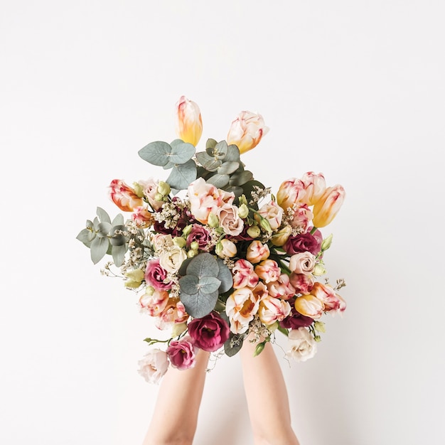 Mão feminina segurando uma tulipa e um buquê de flores de eucalipto contra uma parede branca