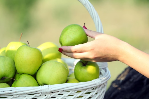 Mão feminina tirando maçã verde da cesta de vime ao ar livre