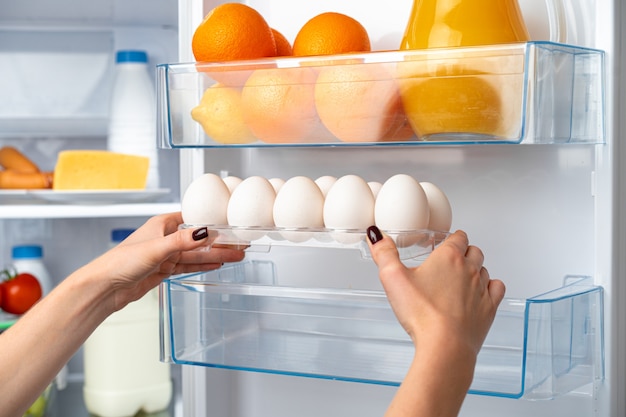 Mão feminina tirando ovo da geladeira close-up