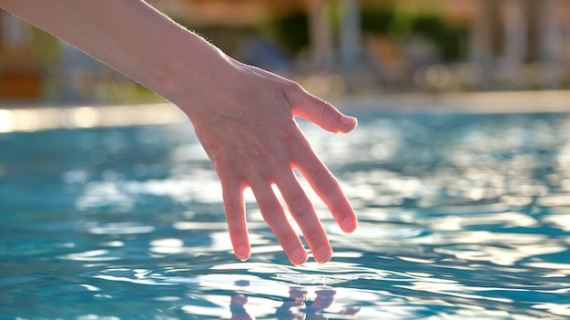 Mão feminina tocando a água da piscina no verão