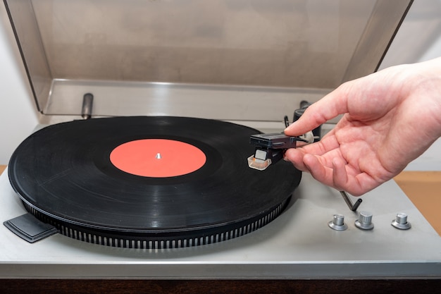 Mão girando em retro vintage analógico de toca-discos estéreo. Uma plataforma giratória de plástico antiquada tocando uma faixa de música, vista frontal. Conceito de música retro