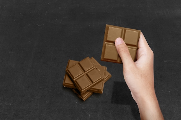 Mão humana com barra de chocolate sobre fundo preto