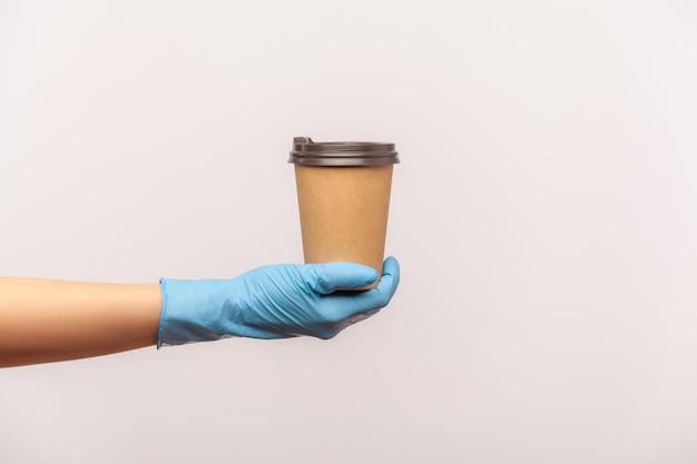 Mão humana em luvas cirúrgicas azuis, segurando e mostrando o copo da bebida quente da caneca para viagem na mão.