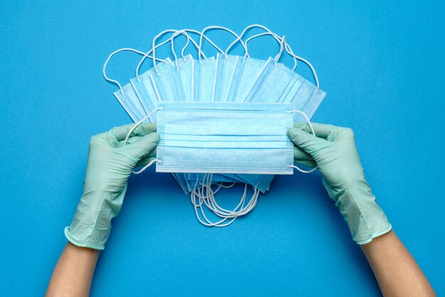 Foto mão humana em luvas de proteção, segurando a máscara protetora facial sobre fundo azul.