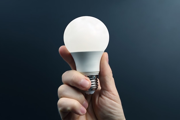 Mão humana segurando a lâmpada led incluída em um escuro. eletricidade e indústria de LED