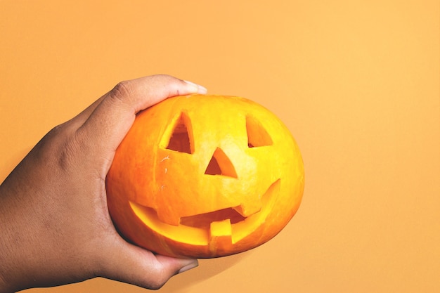 Mão humana segurando Jack-o-Lantern com um fundo colorido