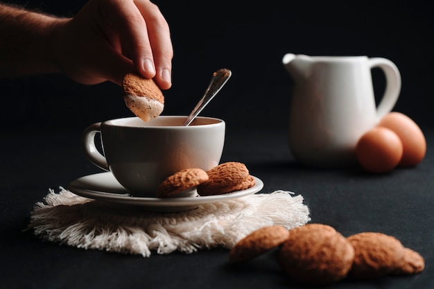 Mão irreconhecível mergulhando um biscoito em café quente, com leite em uma xícara e ovos. Fechar-se