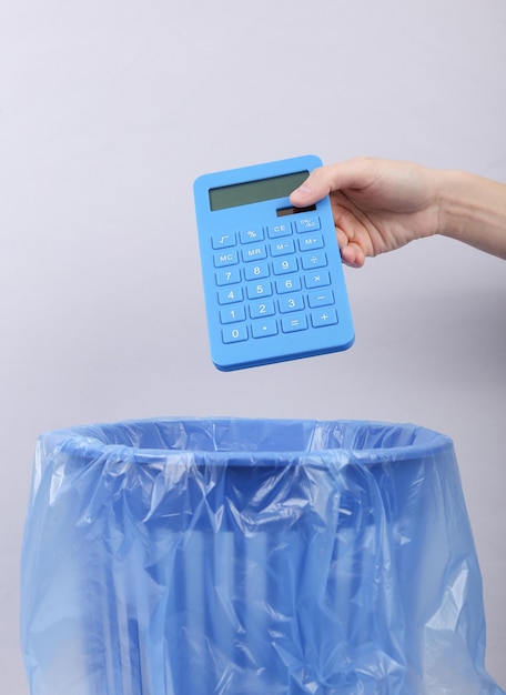 Foto mão joga calculadora na lixeira com pacote em fundo cinza