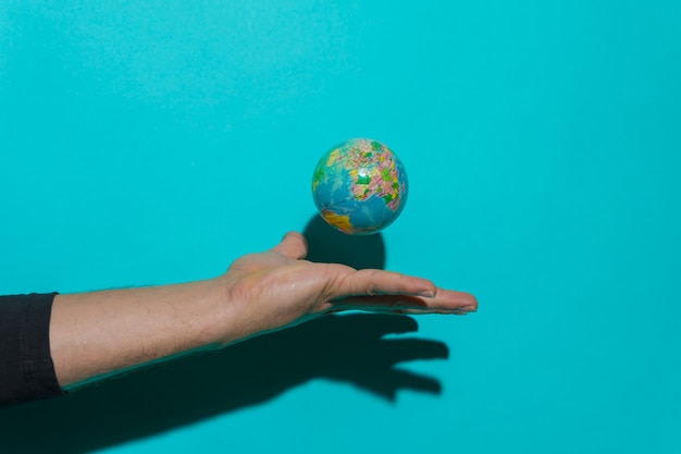 Mão jogando a bola do planeta Terra com fundo azul e copie o espaço para o texto