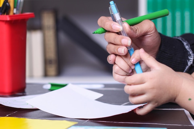 Mão madura ensinando criança a usar a caneta.