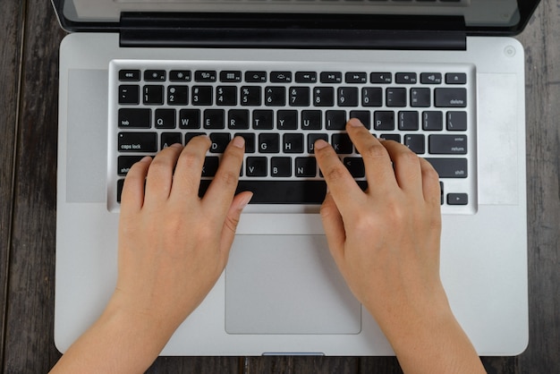 Mão mãos trabalhando em um laptop branco em uma mesa de madeira