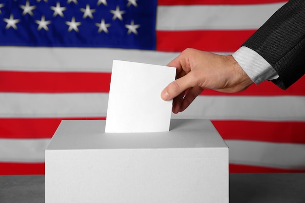 Foto mão masculina colocando cédula de votação na caixa no fundo da bandeira americana