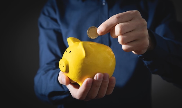 Mão masculina colocando moedas no cofrinho Poupança