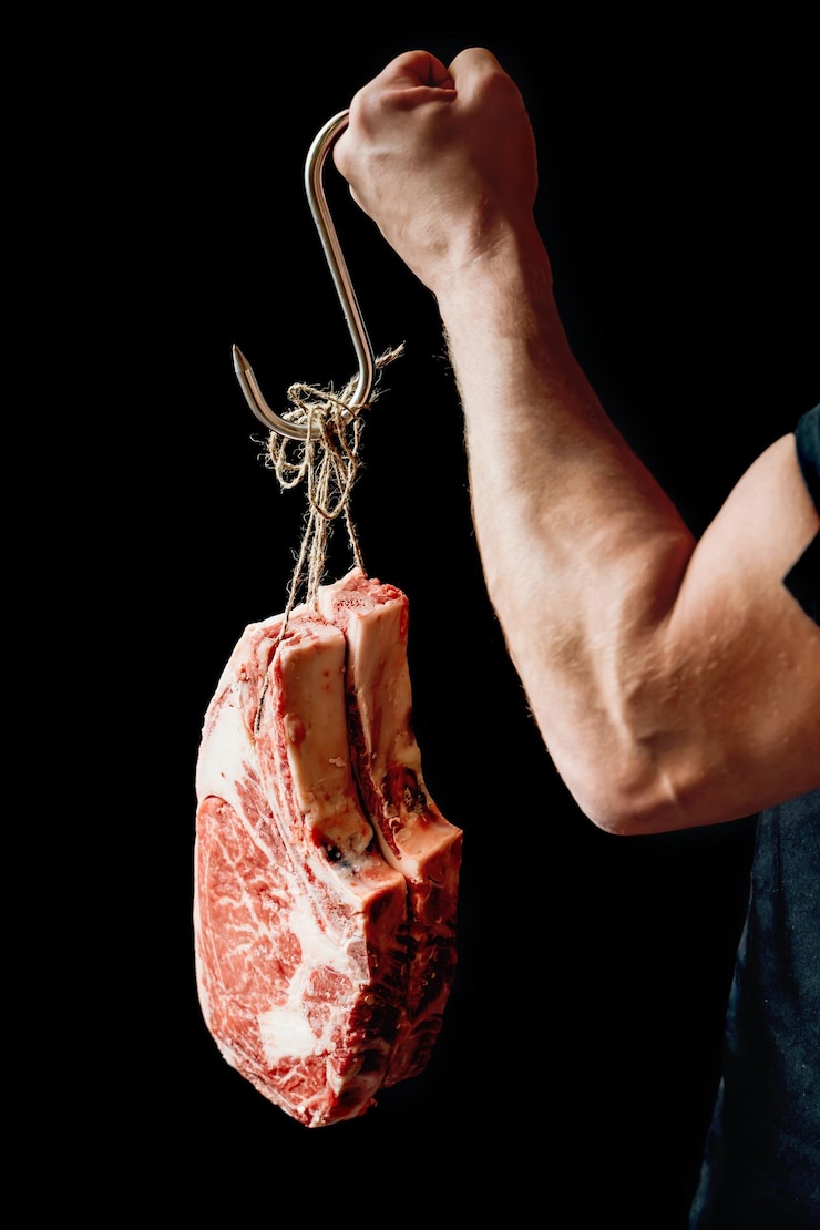Mão masculina de açougueiro forte segurando bifes de carne marmorizada em fundo escuro