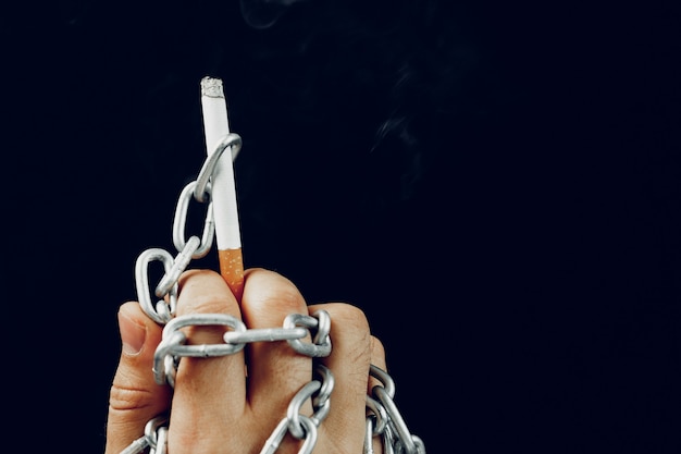 Mão masculina em correntes de metal segurando cigarro, vício de fumar