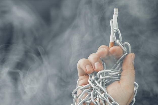 Mão masculina em correntes de metal segurando cigarro, vício de fumar