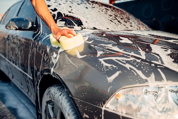 Mão masculina esfregando o carro com espuma, automóvel na espuma. Estação de lavagem de carros