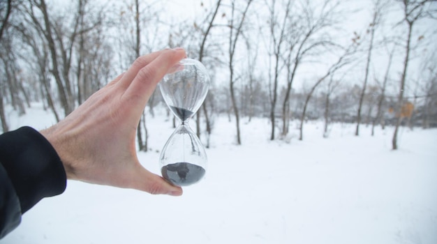 Mão masculina mostrando relógio de areia em fundo de inverno