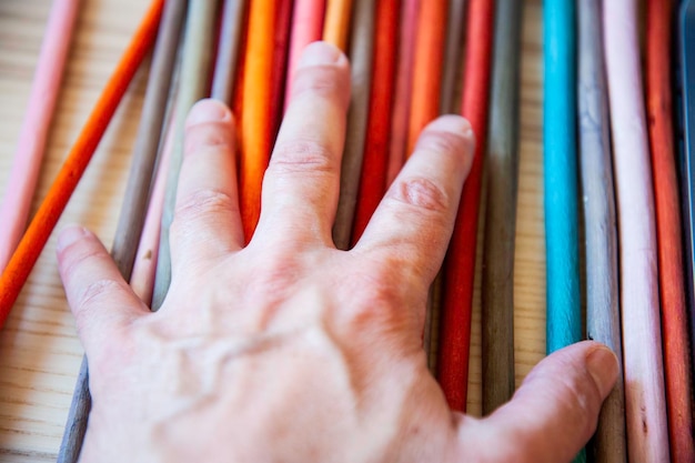 Mão masculina na textura colorida do arco-íris feita de um conjunto de varas de madeira artesanato fácil e ecológico para crianças símbolo de bandeira lgbt Mão masculina em fundo multicolorido Conceito de paz e diversidade