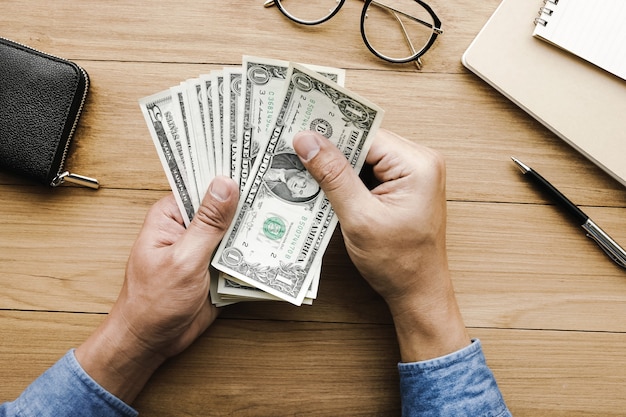 Mão masculina que fura o dinheiro dólar bill.on mesa de madeira.