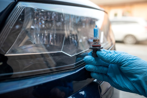 Mão masculina segura uma lâmpada halógena contra os faróis, tudo para consertar o carro