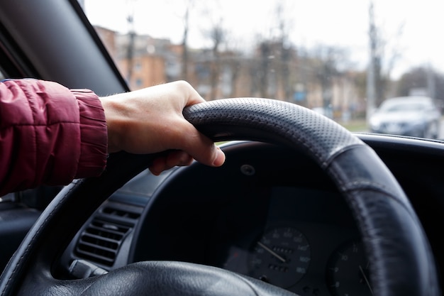 Mão masculina segura volante em couro preto, homem dirigindo, conceito de transporte,