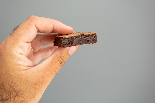 mão masculina segurando brownie de chocolate sobre fundo cinza