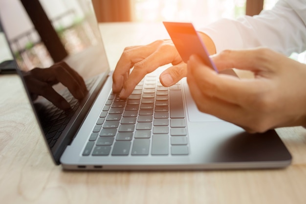 Mão masculina segurando o cartão de crédito e usando o conceito de compras online do laptop