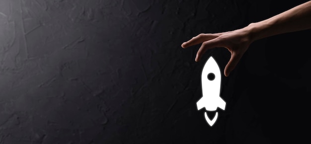 Foto mão masculina segurando o ícone do foguete que decola no foguete de fundo azul está lançando e voando para fora início de negócios marketing de ícones na interface virtual moderna conceito de inicialização