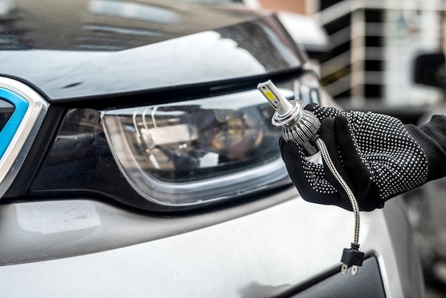 Mão masculina segurando o moderno LED h7 bukb perto do farol de um carro