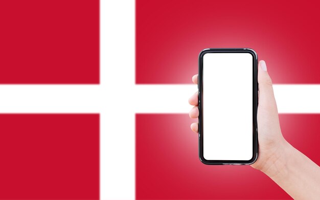 Mão masculina segurando smartphone com espaço em branco na tela no fundo da bandeira desfocada da Dinamarca Closeup view
