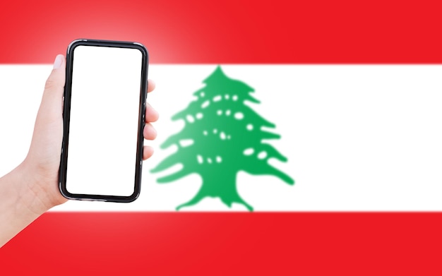 Mão masculina segurando smartphone com espaço em branco na tela no fundo da bandeira desfocada do Líbano Closeup view