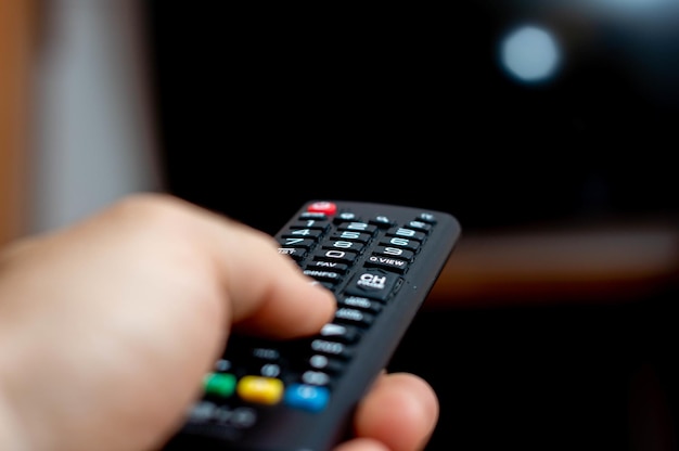 Mão masculina segurando um controle remoto de TV e tentando ligar a TV