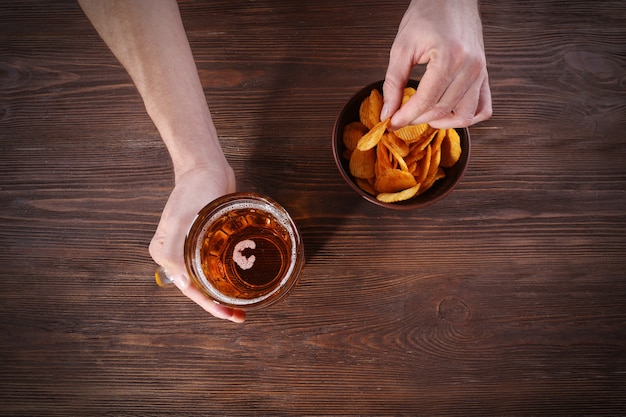 Mão masculina segurando um copo de cerveja na madeira