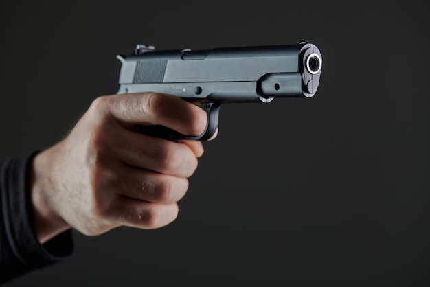 Mão masculina segurando uma arma em fundo preto Uma arma na mão de um homem defesa ou ataque assassino ou ladrão armado Visão em primeira pessoa de uma pistola