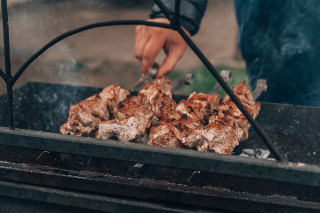 Mão masculina transforma carne crua frita em espetos é cozida na grelha a carvão. cozinhar churrasco ao ar livre