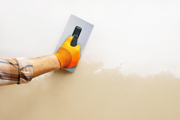 Mão masculina usando espátula e reboco de trabalho no trabalho de reparo de parede em casa