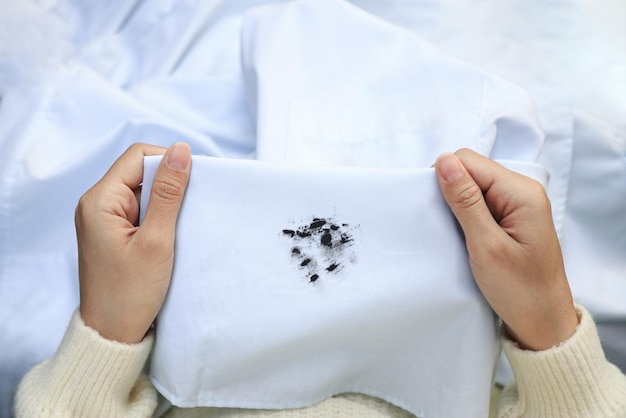 Mão mostrando mancha de tinta preta suja na camisa branca do conceito de mancha de vida diária de acidente inesperado