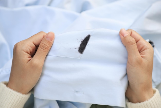 Mão mostrando mancha de tinta preta suja na camisa branca do conceito de mancha de vida diária de acidente inesperado