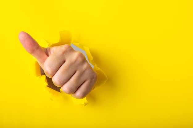 Mão mostrando um sinal de polegar para cima através de um buraco rasgado