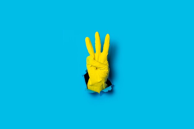Mão na luva amarela mostrando três dedos em um azul brilhante