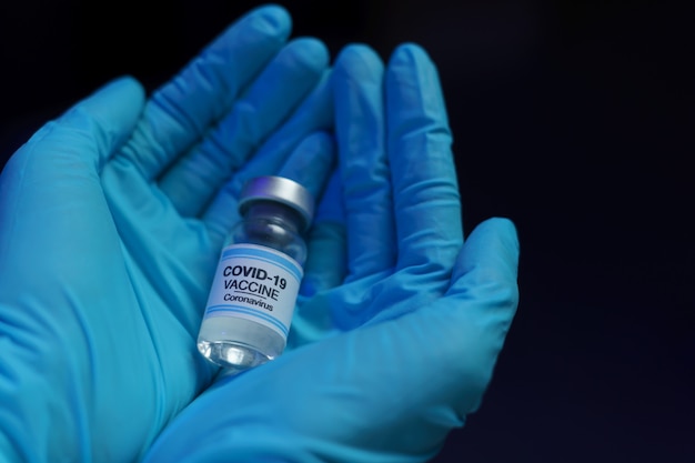 Mão na luva azul segurando a injeção de vacina e seringa para prevenção, imunização e tratamento contra a infecção pelo vírus corona.
