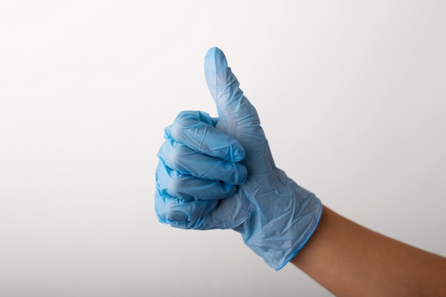Mão na luva azul sobre um fundo cinza mostrando os polegares para cima